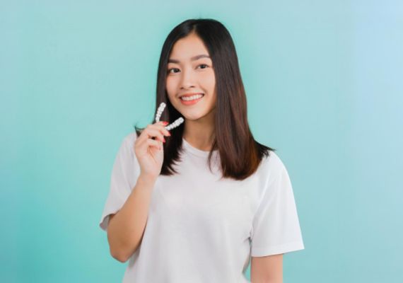 A girl is holding a clear retainer while smiling