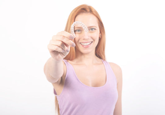 A girl holding a clear retainer in one hand.